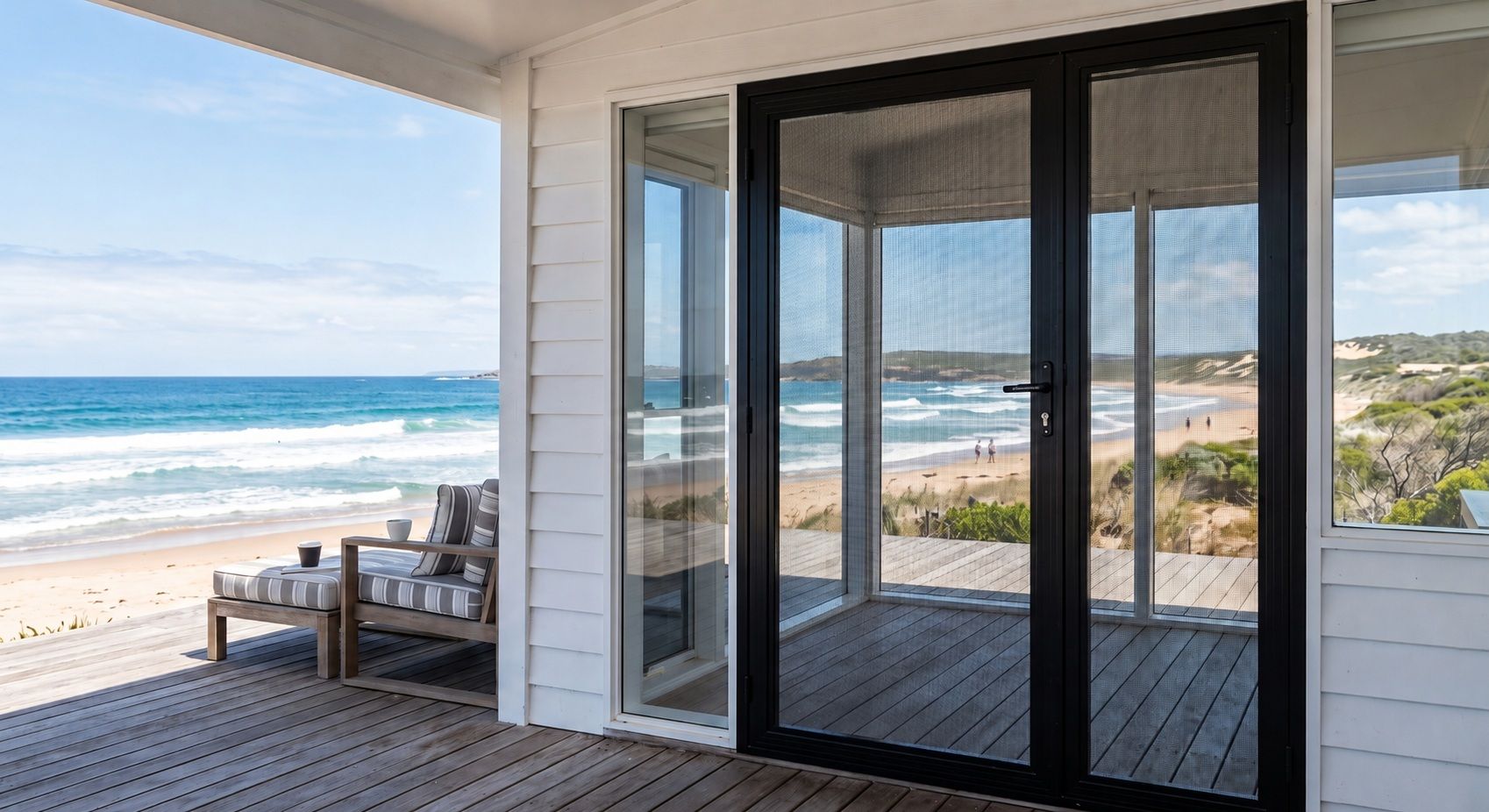 A beachfront home patio with black-framed security screens, outdoor seating, and a view of the ocean and sandy shore.