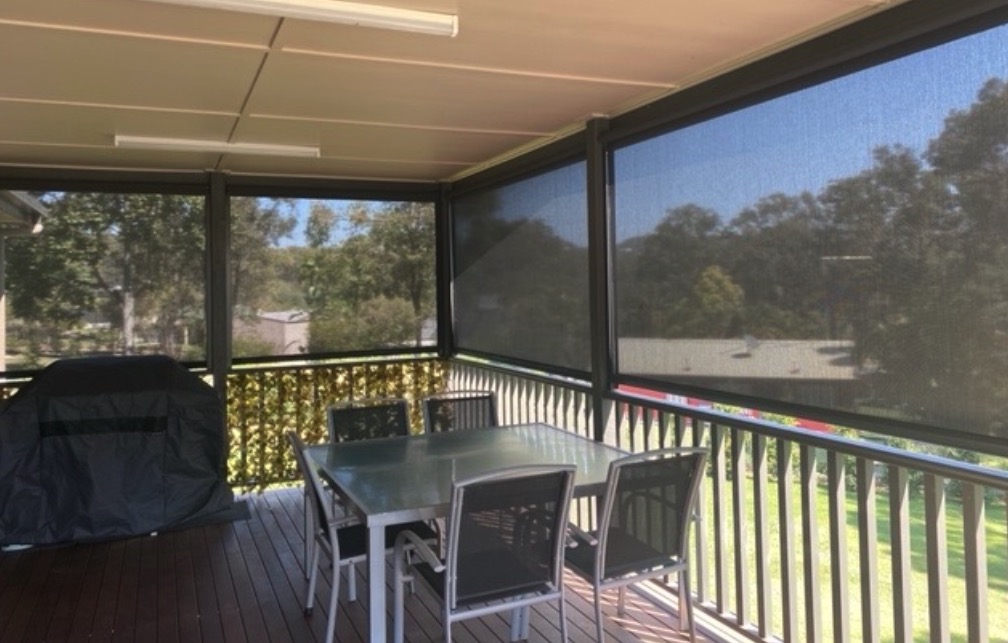 Screened outdoor deck with a dining table, chairs, covered grill, and views of trees and a grassy yard.